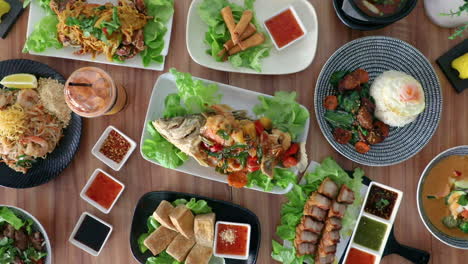 male hand placing thai cuisine fried fish onto flat lay food arrangement