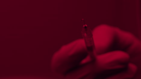 close up of a hand holding a syringe in red light ambience concept of drugs medical pharmaceutical and addiction