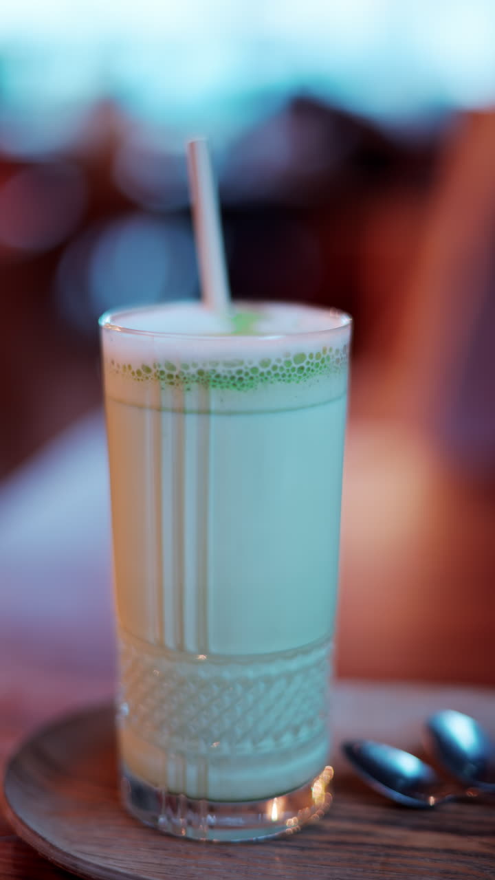 Close up of a matcha latte in a glass with a straw on a table at a cafe. Vertical