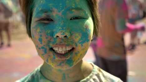 face of young happy asian girl is smiling with colourful powder on holi festival in daytime in summer, color concept, emotional concept