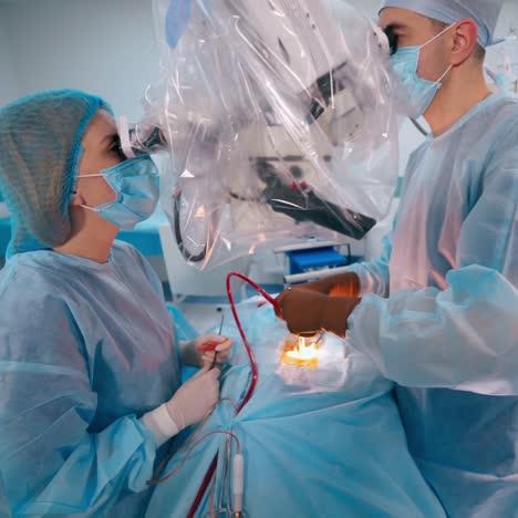 surgeons doing an operation to a patient through the microscope. doctors in blue protective uniform on the modern surgery cabinet background.
