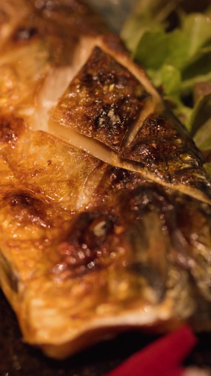 Close-up panning shot of crispy grilled Japanese mackerel served on a ceramic plate.