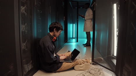 two it specialists coding on laptops in server room