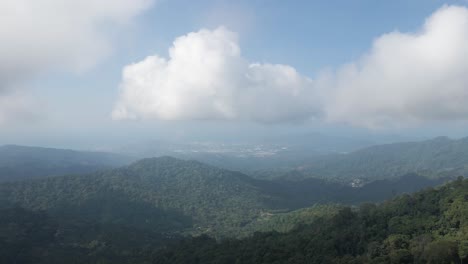 Drone-shot-rises-high-above-the-Sierra-Nevada-mountains-in-Colombia,-to-reveal-the-vast-forested-landscape-with-Santa-Marta-and-the-sea-in-the-distance