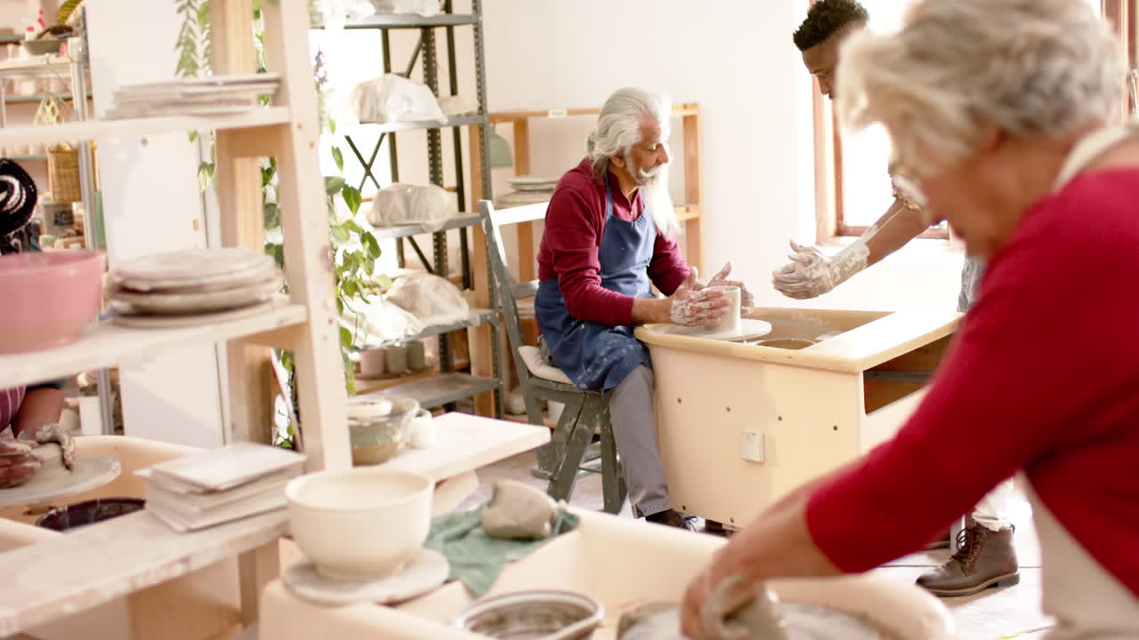 Focused biracial male and female potters using potter's wheel in pottery studio, slow motion