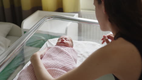 mother looking at sleeping newborn baby in hospital crib