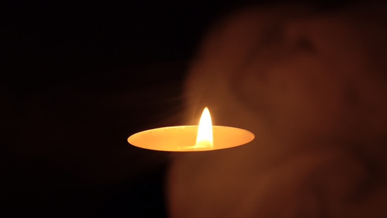 La candela tremola nel buio. Una candela bianca e rotonda brucia su uno sfondo scuro. Candele rotonde bruciano e si spengono. Dolore. Romanticismo. Gioia. Video 4K.