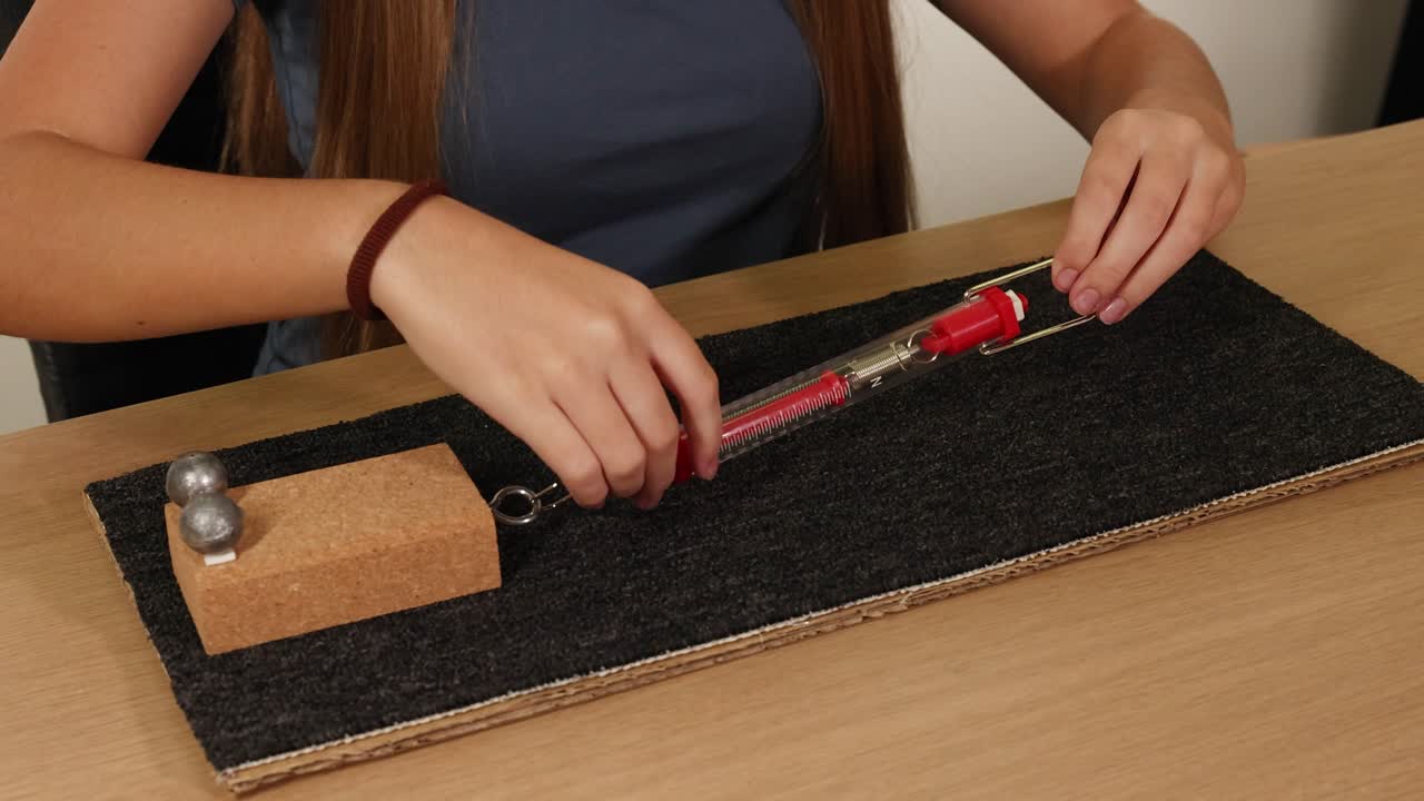 Hands use a spring scale to measure frictional force on a block across a carpeted surface