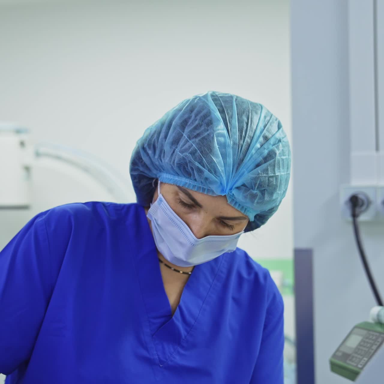 Couple of surgeons operate the patient in highly-equipped operational room. Female assistant checks the medicines in drop counter