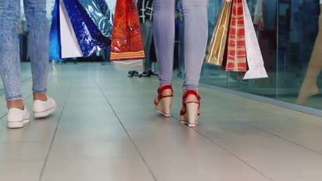 dos mujeres con bolsas de compras están en la vista trasera del centro comercial solo las piernas visibles video hd