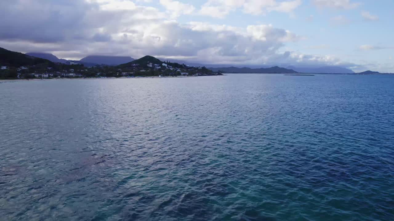 imágenes de drones a través del océano pacífico azul profundo cerca de la playa de lanakai oahu hawai con playa de arena blanca y residencias enclavadas entre las montañas de la selva tropical y el océano