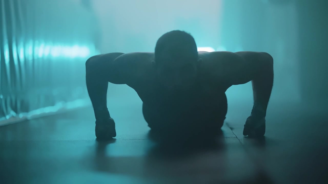 Silhouette of a Muscular Man Doing Push-ups in a Dark Gym with Blue Light