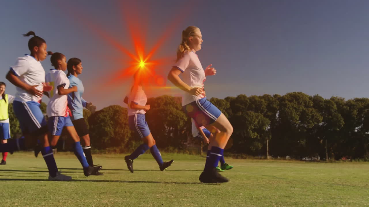 Practicing soccer on field, players in blue shorts with bright red lens flare
