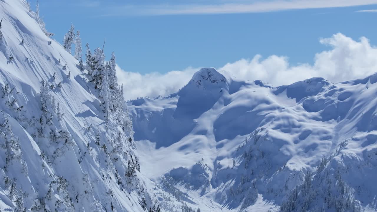 Expansive aerial shot of a cliffside with a mountain range in the background covered in snow