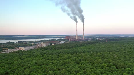aerial view on the green forest and pipes with smoke from plant. natural landscape of woodland near the river and industrial factory on the bank of the river.