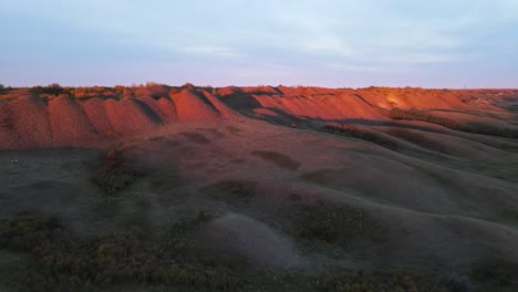 sol vespertino rojo golpeando las puntas de algunas colinas redondas en las tierras baldías canadienses
