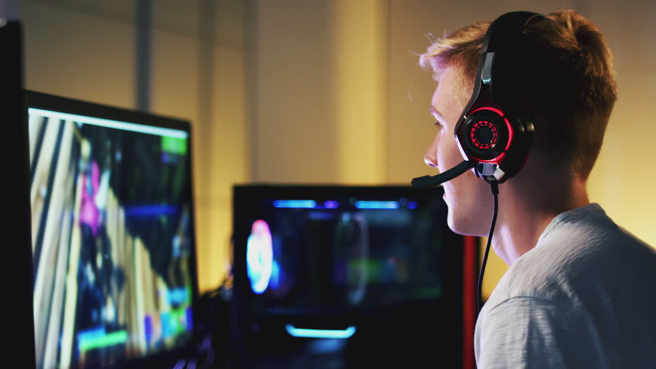 Teenage Boy Wearing Headset Gaming At Home Using Dual Computer Screens