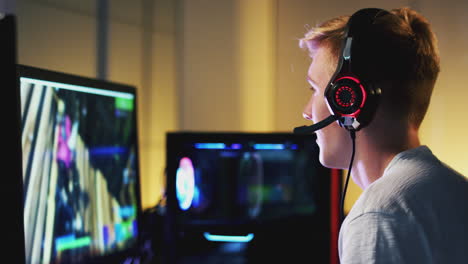 teenage boy wearing headset gaming at home using dual computer screens