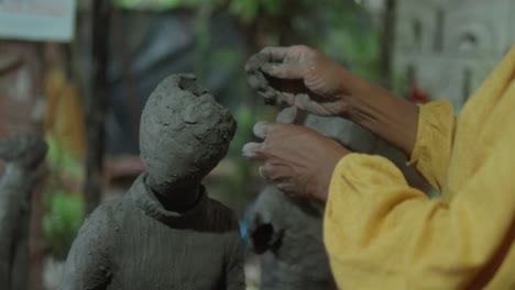 a close-up of an artisan's hands carefully sculpting the facial features of a clay idol