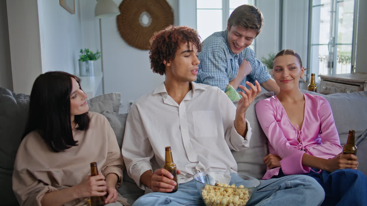 Curly guy talking friends sitting couch at living room. People watching sitcom