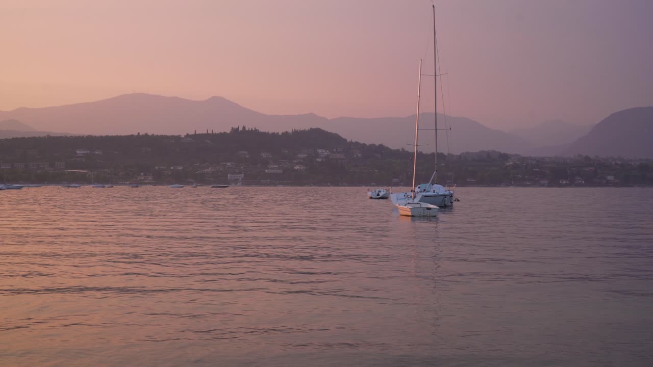 красивая вечерняя сцена на озере гарда в северной италии: парусники качаются на анкоре