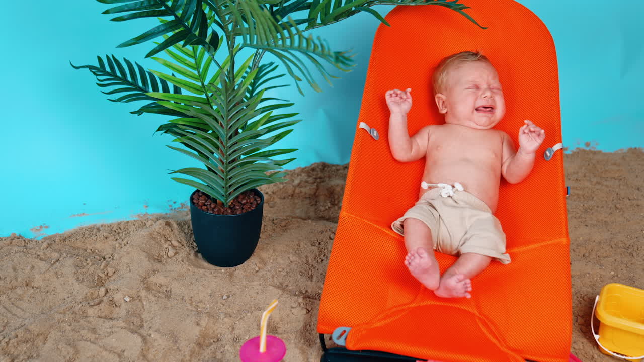 Tiny Caucasian infant lying in the baby chair starting to cry. Newborn boy resting in the beach.