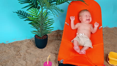 tiny caucasian infant lying in the baby chair starting to cry. newborn boy resting in the beach.