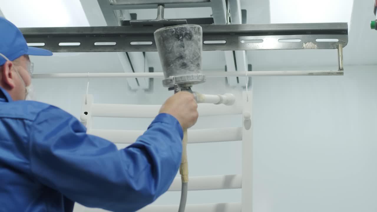 A worker paints a stainless steel metal structure with an airbrush spray gun. Dry painting method.