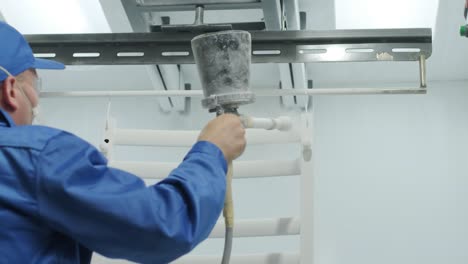 un trabajador pinta una estructura metálica de acero inoxidable con una pistola de pulverización de aerógrafo. método de pintura en seco.