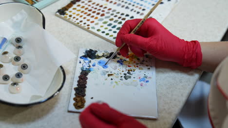 master is painting artificial eye. medical technician uses colors and special brush for making eye prosthesis.
