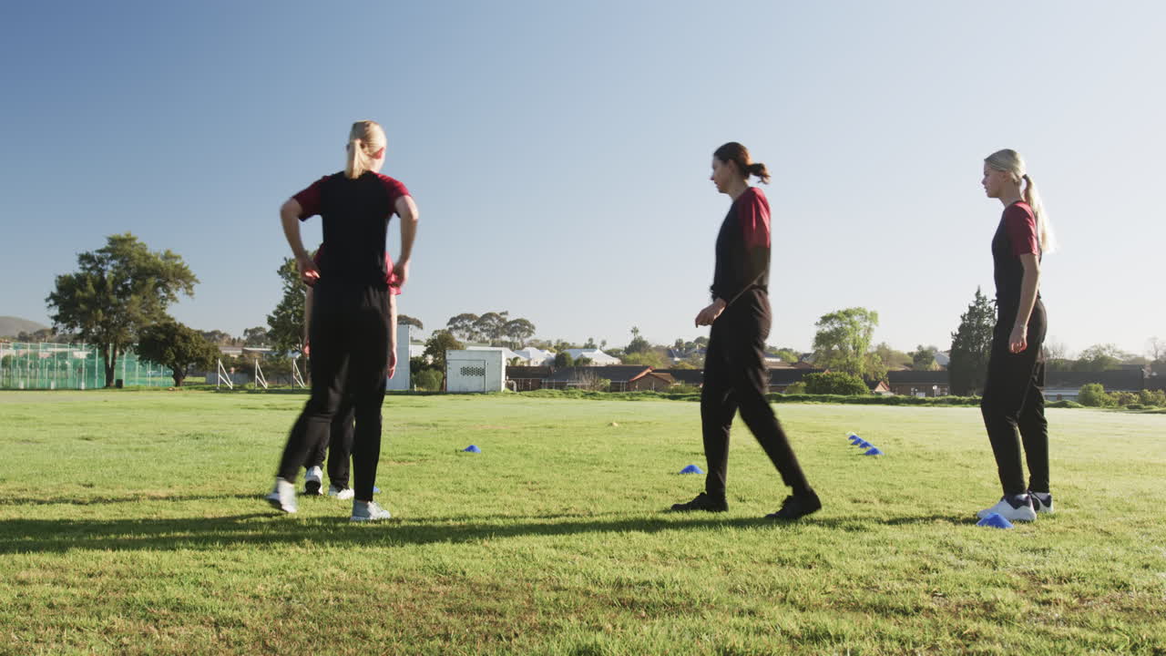 Playing cricket, women practicing drills on field, wearing sports uniforms