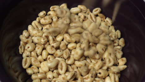 primer plano de la parte superior del cereal de trigo y miel que cae en un tazón morado vacío