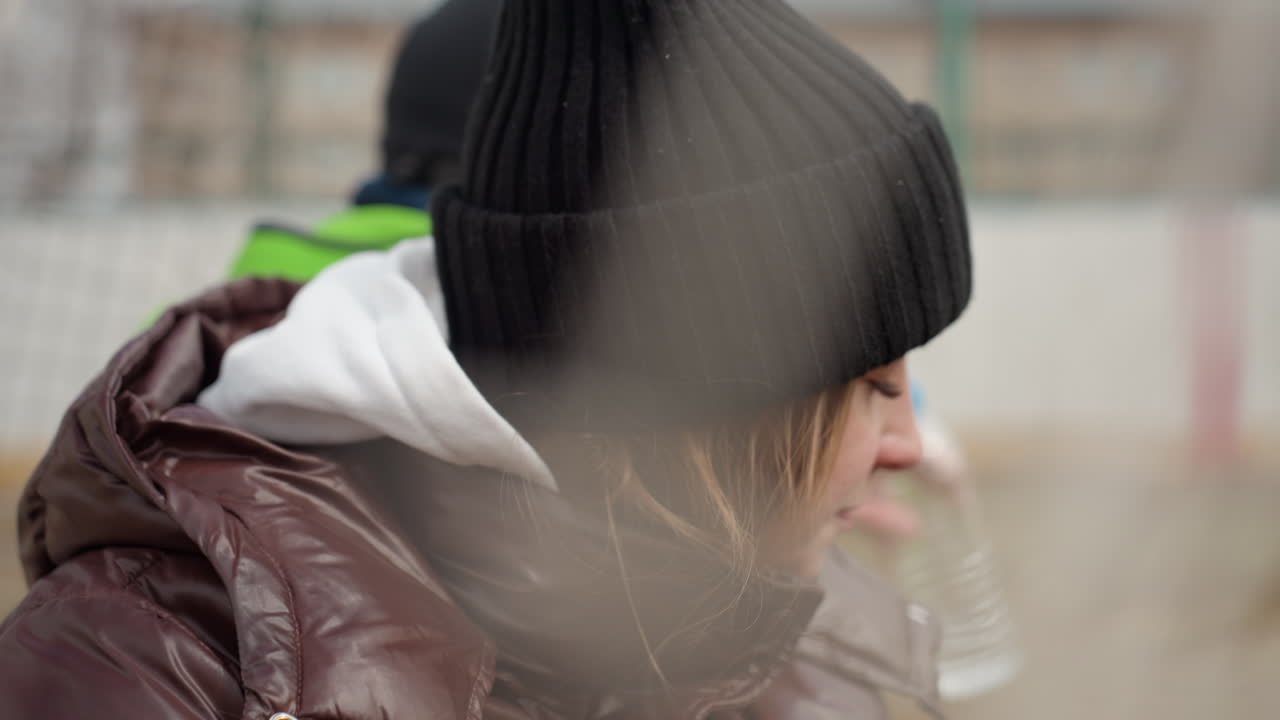 겨울에 보이는 사람, 겨울옷을 입은 사람이 멀리서 조용히 운동 경기를 관찰하고, 두꺼운 겉옷을 입고 반사적인 태도를 보이는 사람이 야외 스포츠 장면을 지켜보고 있어요.