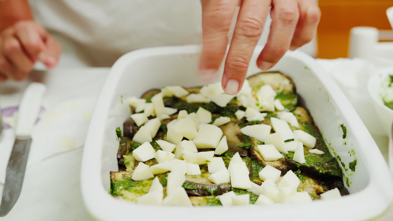 Le mani di una donna che prepara una lasagna di melanzane e provola