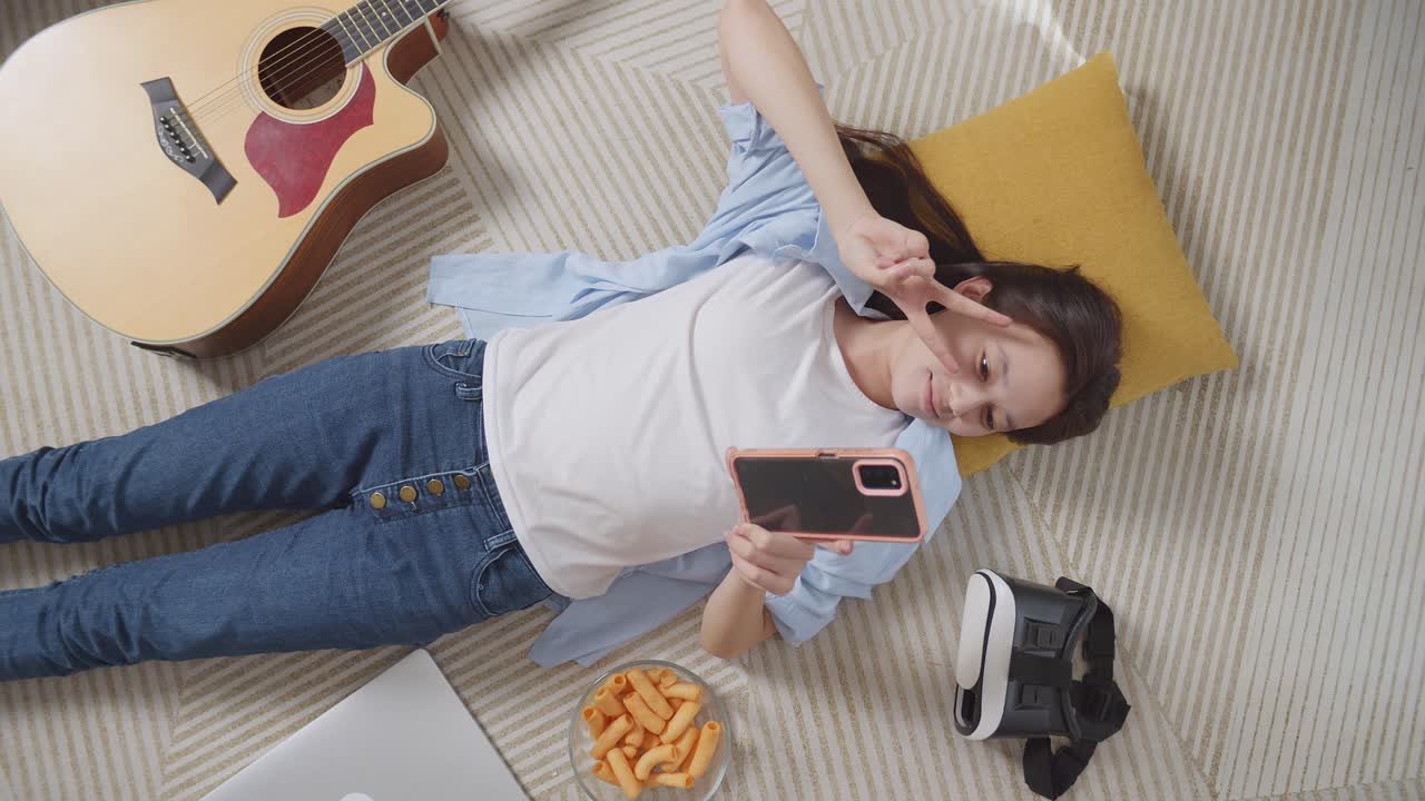 집에서 바닥에 카에 누워서 셀피를 찍는 스마트폰을 사용하는 아시아 십대 소녀의  뷰. 웃음, 평화와 마음의 몸짓을 보여주는