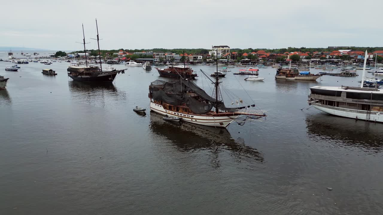 Luftdrone-scene av seilbåter i tre fortøyd i havneområdet på Bali, som viser rolige, tropiske forhold, jevne vannoverflater og klassiske maritime båter som hviler i den stille havnen
