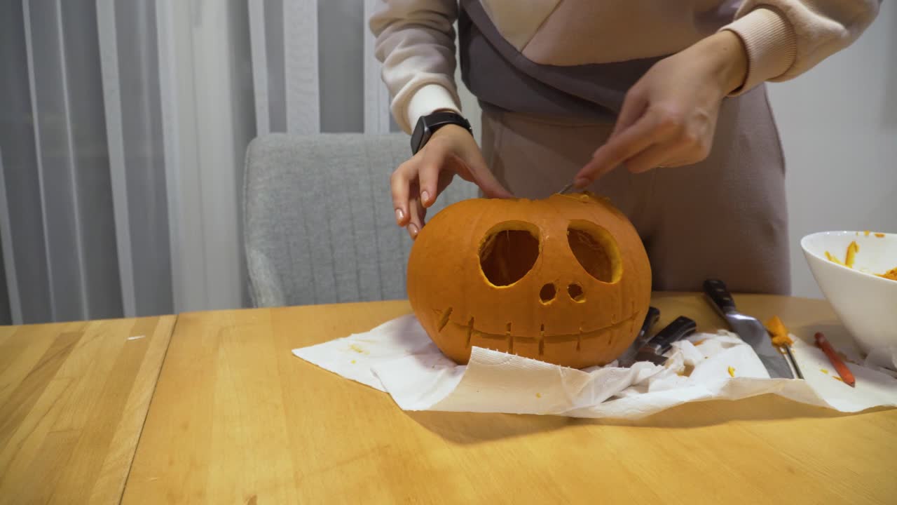 primer plano deslizante de una mujer joven tallando calabaza naranja en casa para la decoración de halloween, está limpiando la calabaza de las semillas