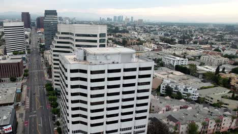 Edificios-En-El-área-De-Brentwood-De-Los-Ángeles-A-Lo-Largo-De-Wilshire-Boulevard---Vista-Aérea-Ascendente-En-Una-Mañana-Brumosa-Con-El-Horizonte-De-La-Ciudad-En-La-Distancia