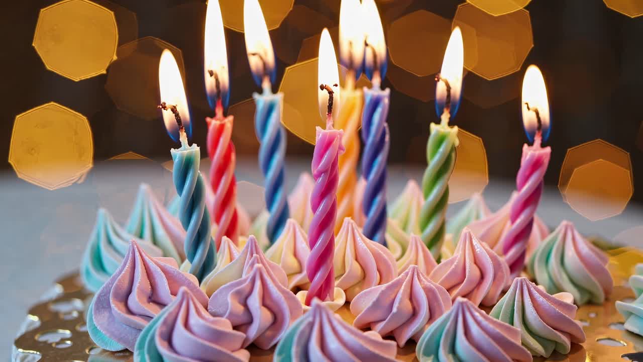 Colorful birthday candles on a cake with pastel meringues, captured from a low angle