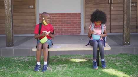 niño y niña comiendo el almuerzo de la caja de tiffin mientras están sentados en un banco en el parque en la escuela
