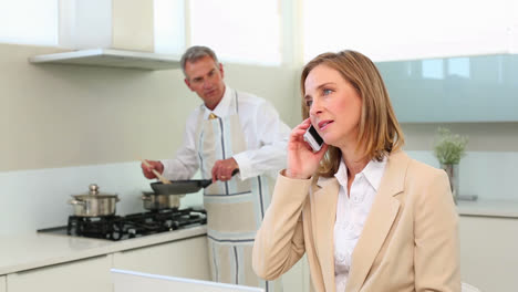 businesswoman talking on phone while husband cooks dinner