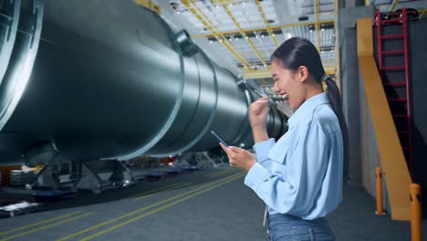 side view of happy asian business woman celebrating using mobile phone in pipe manufacturing factory