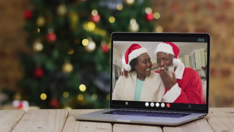 Pareja-De-Ancianos-Afroamericanos-Con-Sombreros-De-Santa-En-Videollamada-En-Una-Computadora-Portátil,-Con-árbol-De-Navidad