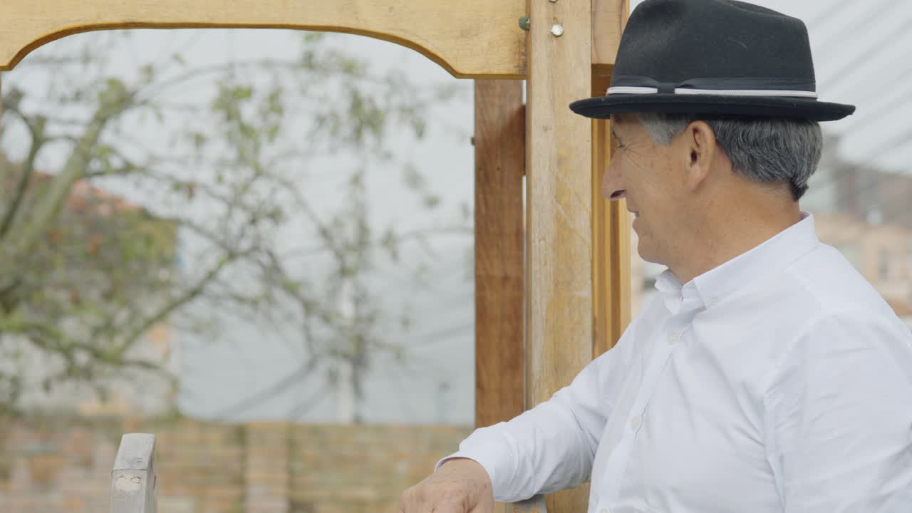 A tender moment between a grandfather and his grandson as they play in a wooden playhouse with a slide in their backyard. The boy happily slides down while the grandfather happily accompanies him.