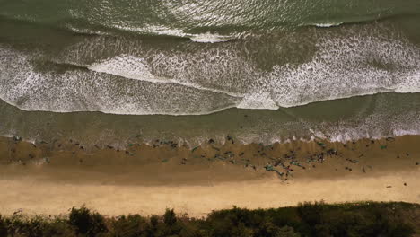 Aerial-top-down-ocean-waves-crashing-on-sandy-tropical-beach-with-plastic-fisherman-net-during-monsoon-season-in-Vietnam