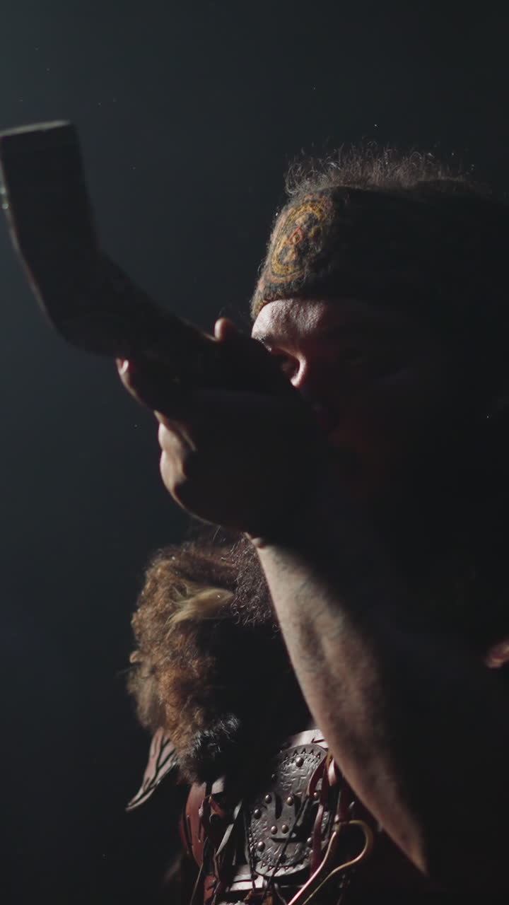 Plump man in Altai shaman costume draws in large smoking pipe in dark studio closeup. Ritual of communication with ancestor. Folk mystic