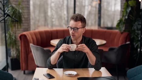 un joven elegante sentado en un café recibe un mensaje alegre en un teléfono inteligente