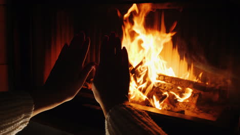 woman warms her hands by the fire of a fireplace at home