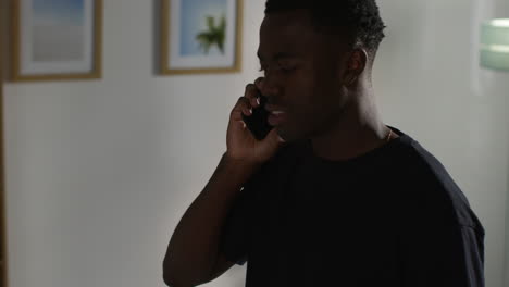 angry young man standing in lounge at home having argument talking on mobile phone