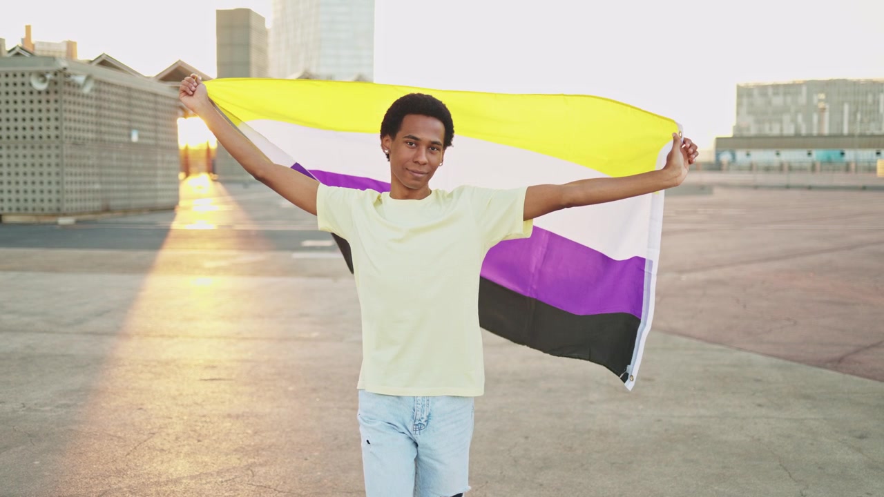 Pessoa Jovem Não-Binária Segurando com Orgulho a Bandeira do Orgulho Não-Binário ao Pôr do Sol